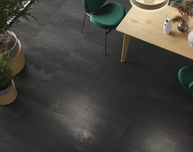 Black metalllic rectangle porcelain tiled kitchen floor with light wood table and green chairs and plants in corner of room