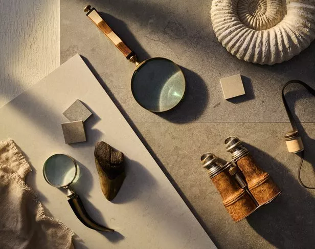 Various pieces of tile and mosaics laid out randomly with magnifying glasses, vintage binocular, and fossils.