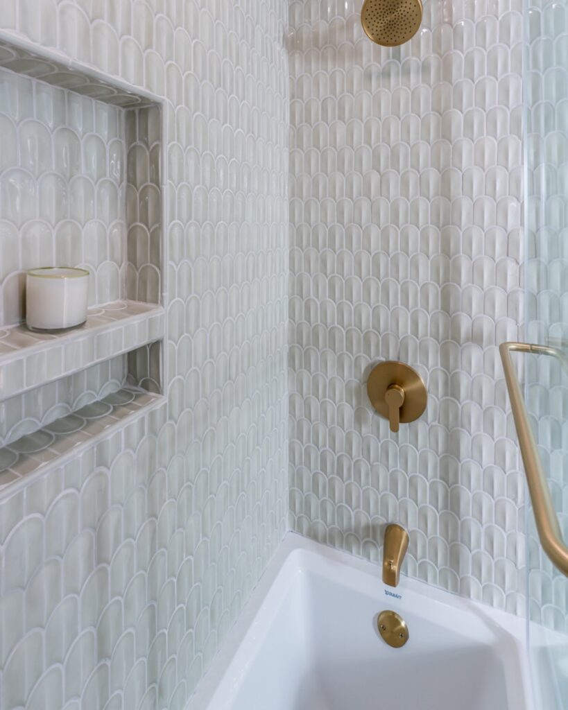 White 3D scallop shaped ceramic mosaic tiles in a shower with niche and gold fixtures.