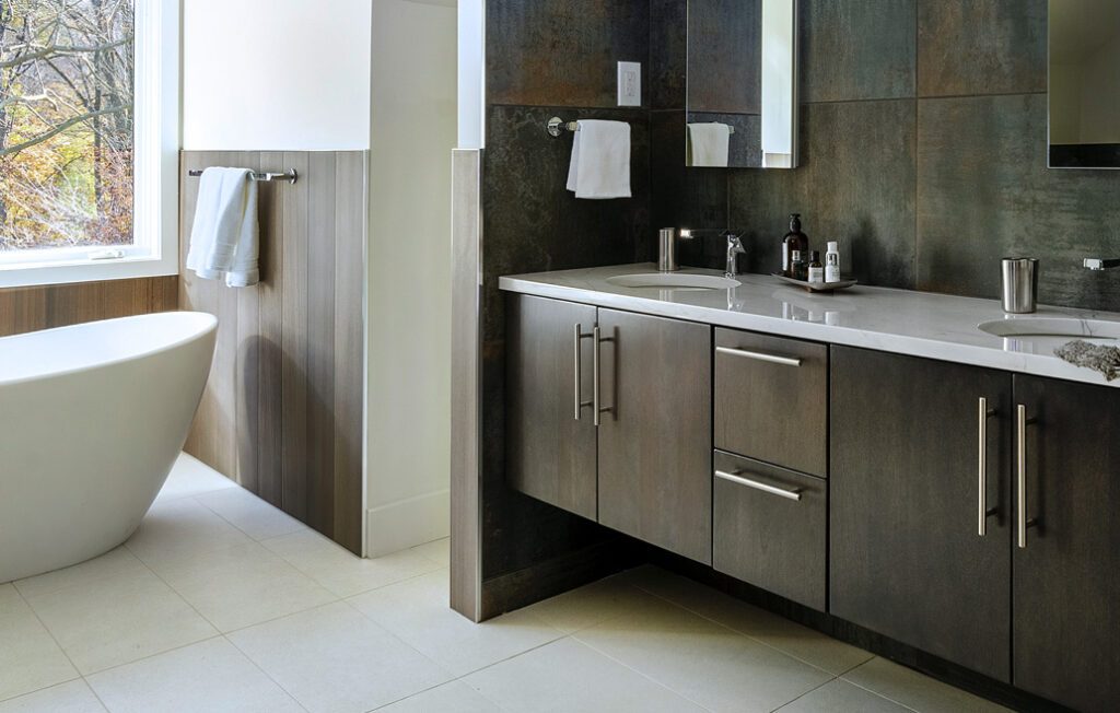 bathroom with white tiles on floor, metallic tiles on wall, wood-look tiles surrounding soaking tub and dark brown cabinet with double sink adn white marble countertop