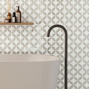 Beige and white square tiles with a petal pattern on a bathroom wall with soaking tub, floor mount faucet, and floating shelf