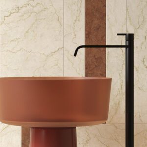 Ivory marble tiled bathroom wall with terracotta colored pedestal sink and black floor mount faucet