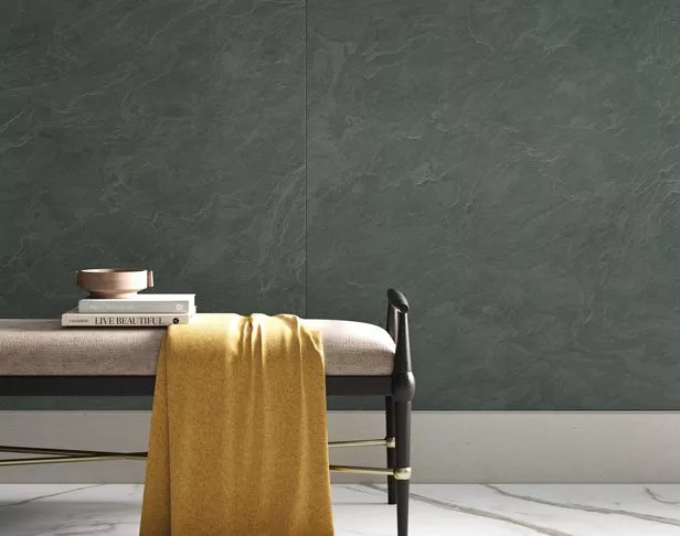 Large green slate-look porcelain paneled wall with cushioned bench, gold throw, and books