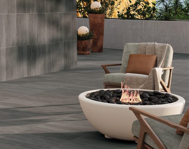Gray tiled patio with matching wall with round modern fire pit and two comfy chairs