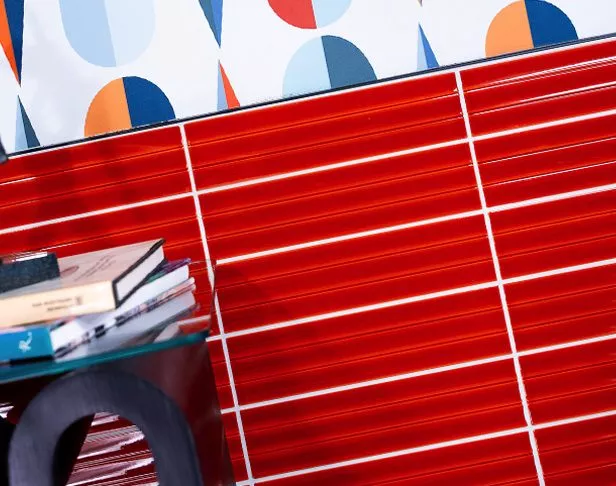 Bold orange fluted ceramic wall tiled wall with colorful wallpaper, black side table with books