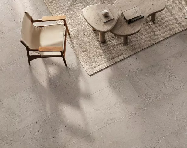 Light gray fossilized porcelain tiled floor with beige sitting chair, accent tables, and jute rug
