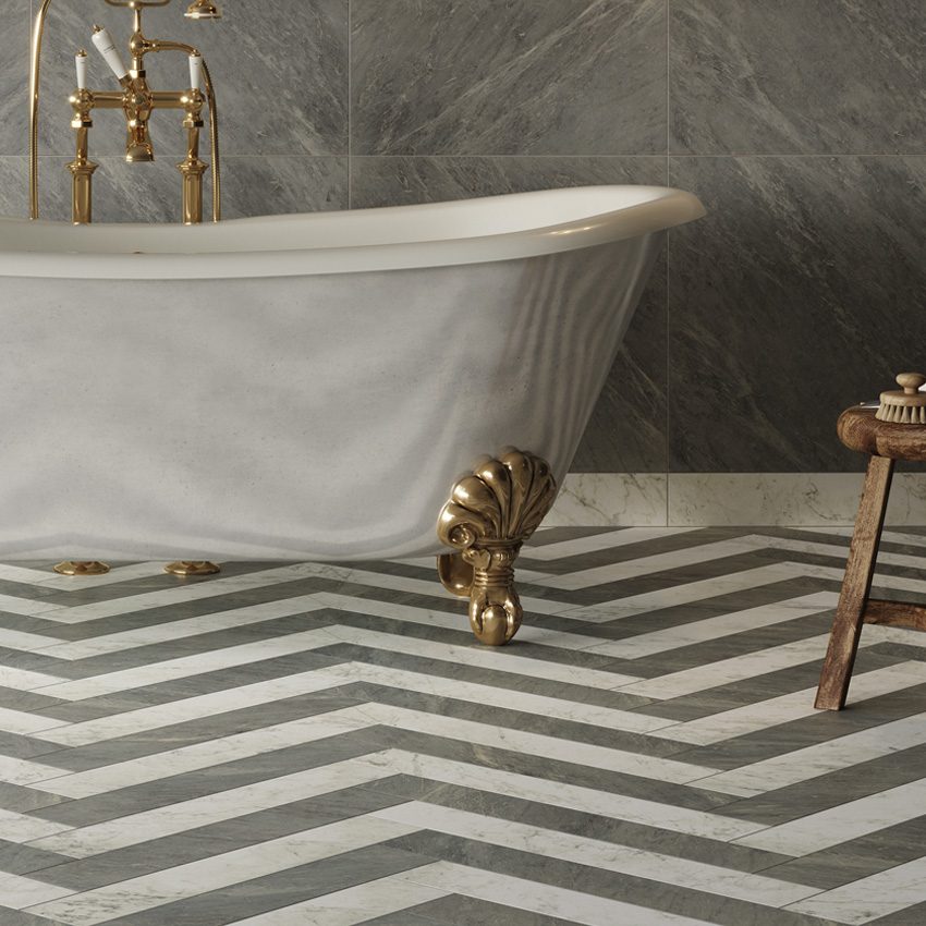 Gray and white marble-look porcelain tile installed in a herringbone pattern on the floor and gray marble-look tile on the wall with gold claw-footed tub and gold fixtures