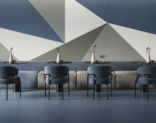 Large blue, gray, and white porcelain panels in a triangular pattern on a cafe wall with service tables and chairs