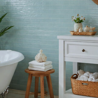 Aqua blue 3x24 glossy porcelain tiled bathroom wall with white clawfoot tub, white vanity, and vintage wood stool with towels