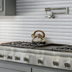 White marble look linear mosaics on a kitchen backsplash with professional stainless steel stove and teapot