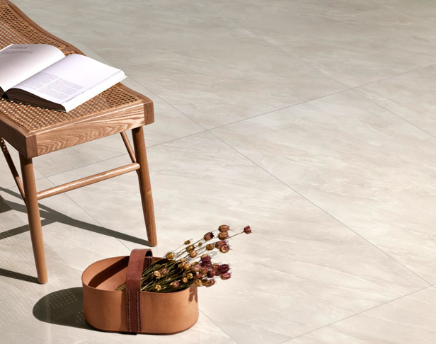 Beige onyx look porcelain polished tiled floor with rattan chair, book, and dried flowers