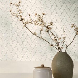 Beige Marble look braided mosaics on a wall with pudgy gray vase with cherry bloosom twigs