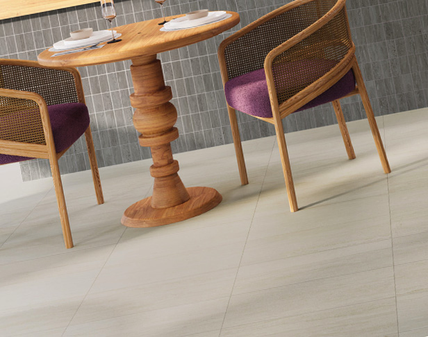 Rugged stone-look White porcelain tiled floor and grey 2x4 mosaic tiled counter in a cafe with light wood pedestal table and cushion chairs