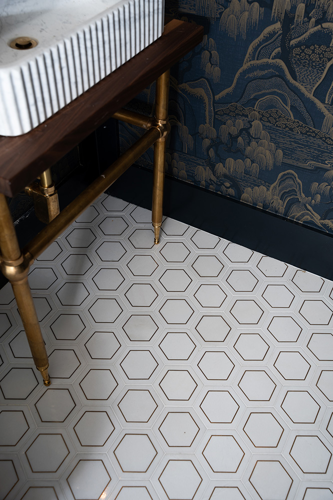 White hexagon floor tiles with gold accents on a bathroom florr with brass legged sink vanity and white marble sink