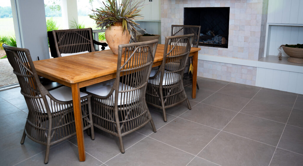Finished basement leading to an outdoor patio with gray porcelai tiles on the floor, rattan dining room set, and tiled fireplace.