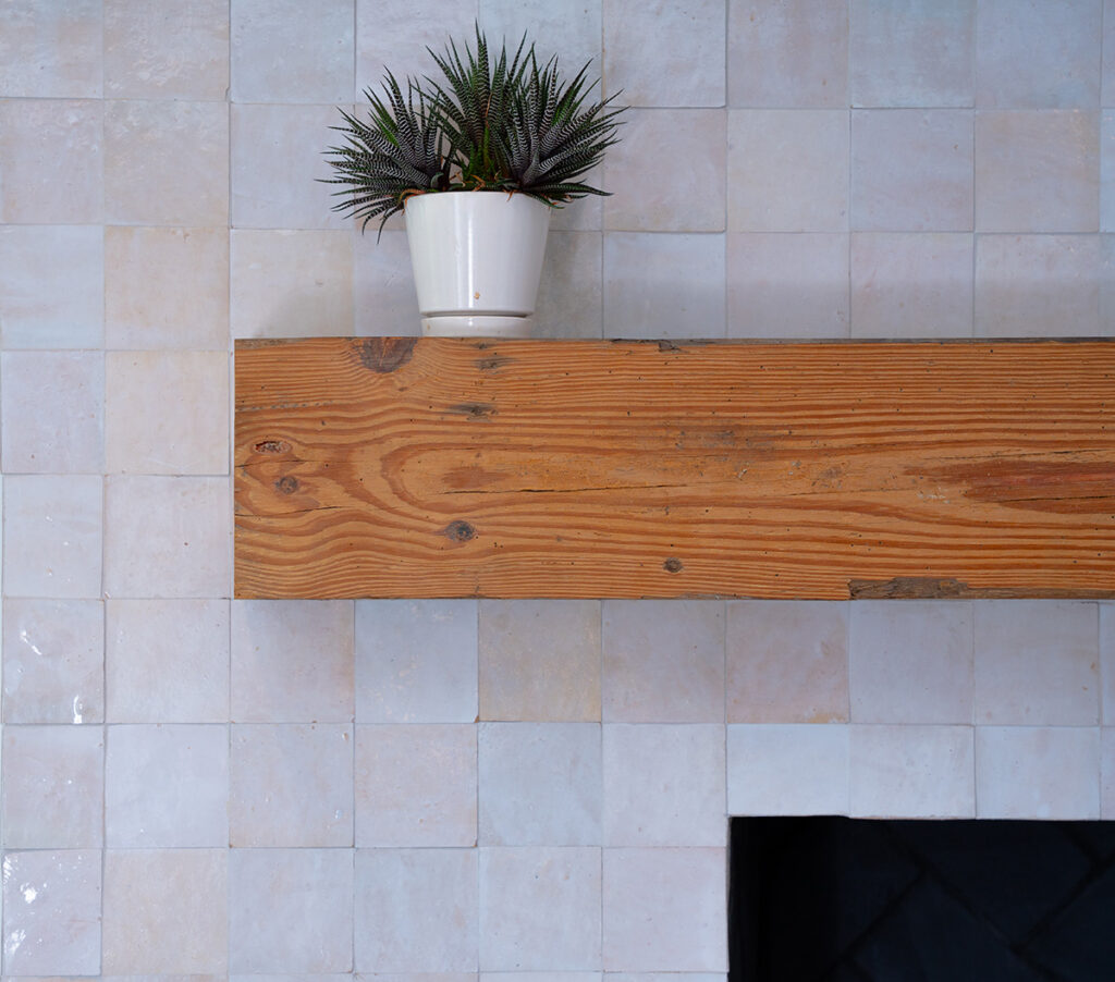 Beige glossy hand-made tiledd fireplace with wood mantle and plant