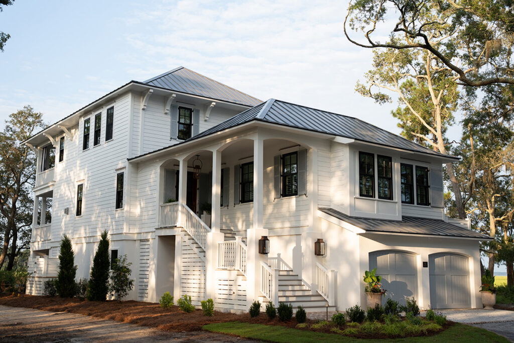 Large coastal home with double garage and stairs with white railing and landscaping detail