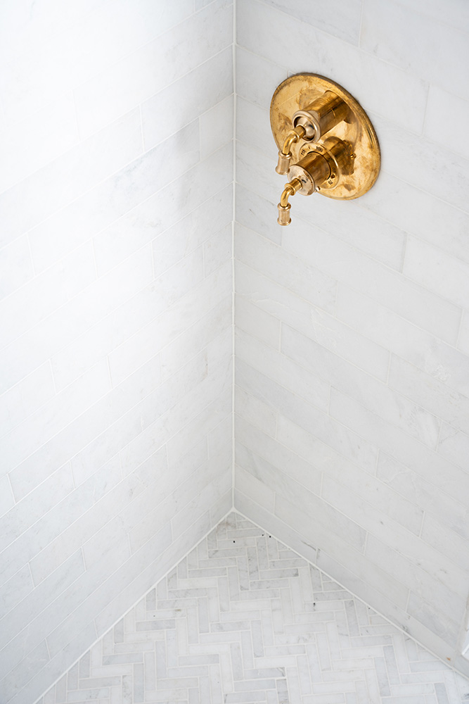 White marble tiled shower with herringbone mosaics on shower floor and gold fixtures