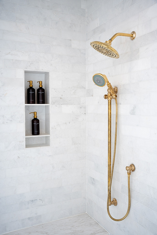 White marble tiled shower with wall niche and gold fixtures