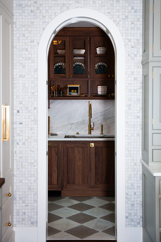 Arched doorway leading into a pantry with checkerboard tiled floor, brown wood cabinets, and marble backsplash