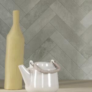glossy gray small format tiled wall in a herringbone pattern with tall slender yellow vase and white tea pot
