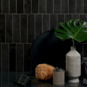 Glossy black small format tiled wall with white vase, sea sponge, and candle