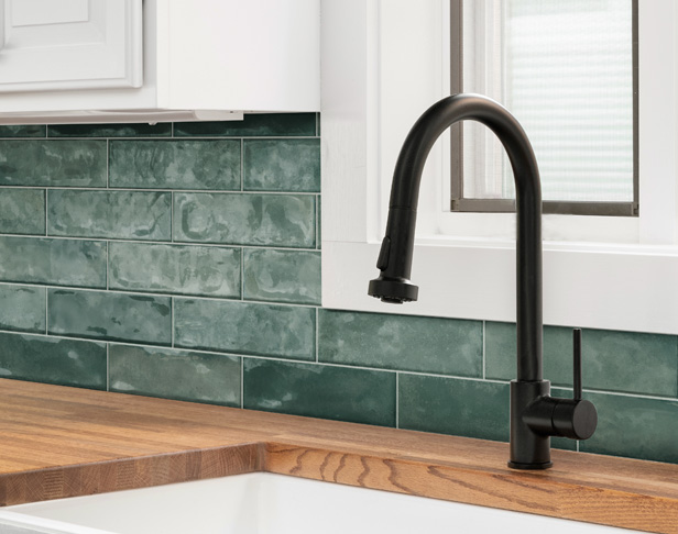Green 3x12 tiled kitchen backsplash with white cabinets and black faucet