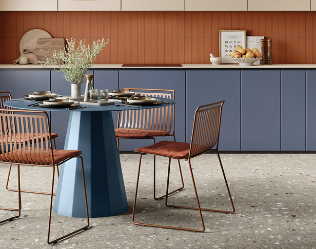 Gray terrazzo-look tiled kitchen floor with terracotta colored subway tiled backsplash with modern dinette set and blue cabinets