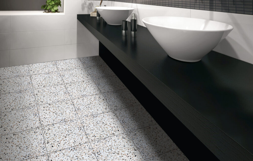 Salt and pepper colored terrazzo tiled bathroom floor with black vanity with white vessel sinks